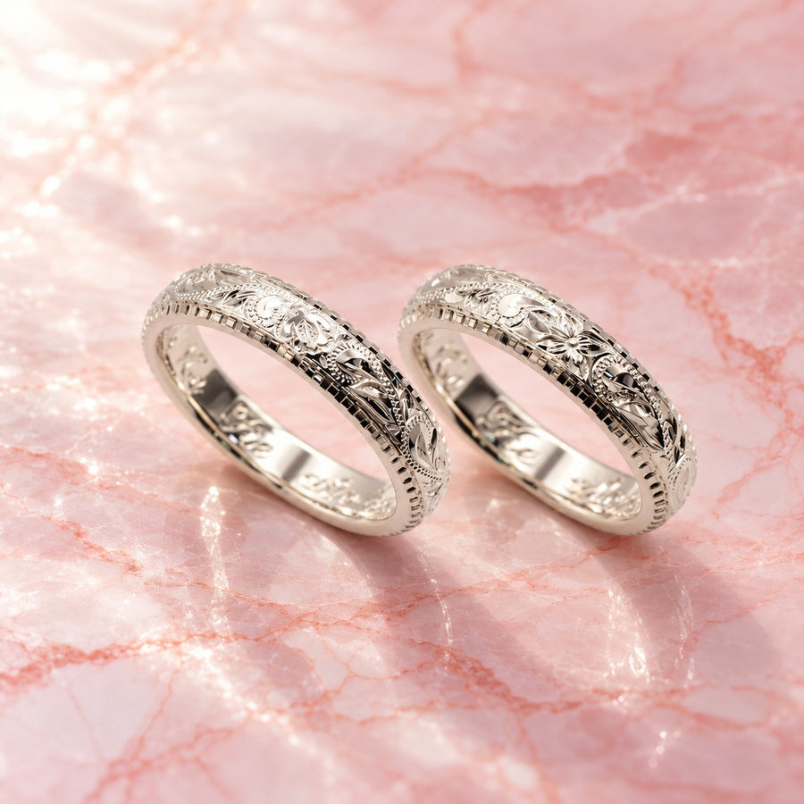 ピンクの大理石の上に並べた、ヘリテージスクロールを彫ったシルバーの結婚指輪2本